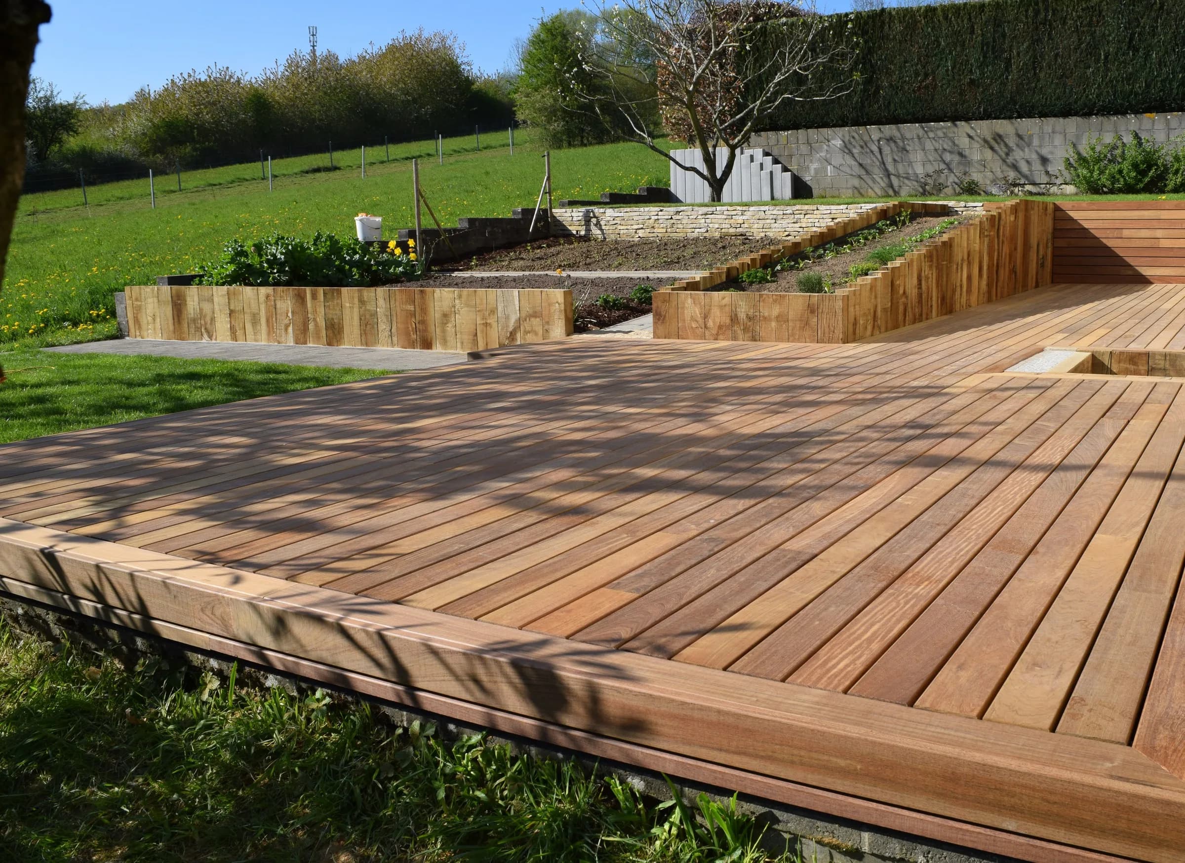 Terrasse en bois exotique et massifs bordés de traverses, ouverts sur la prairie
