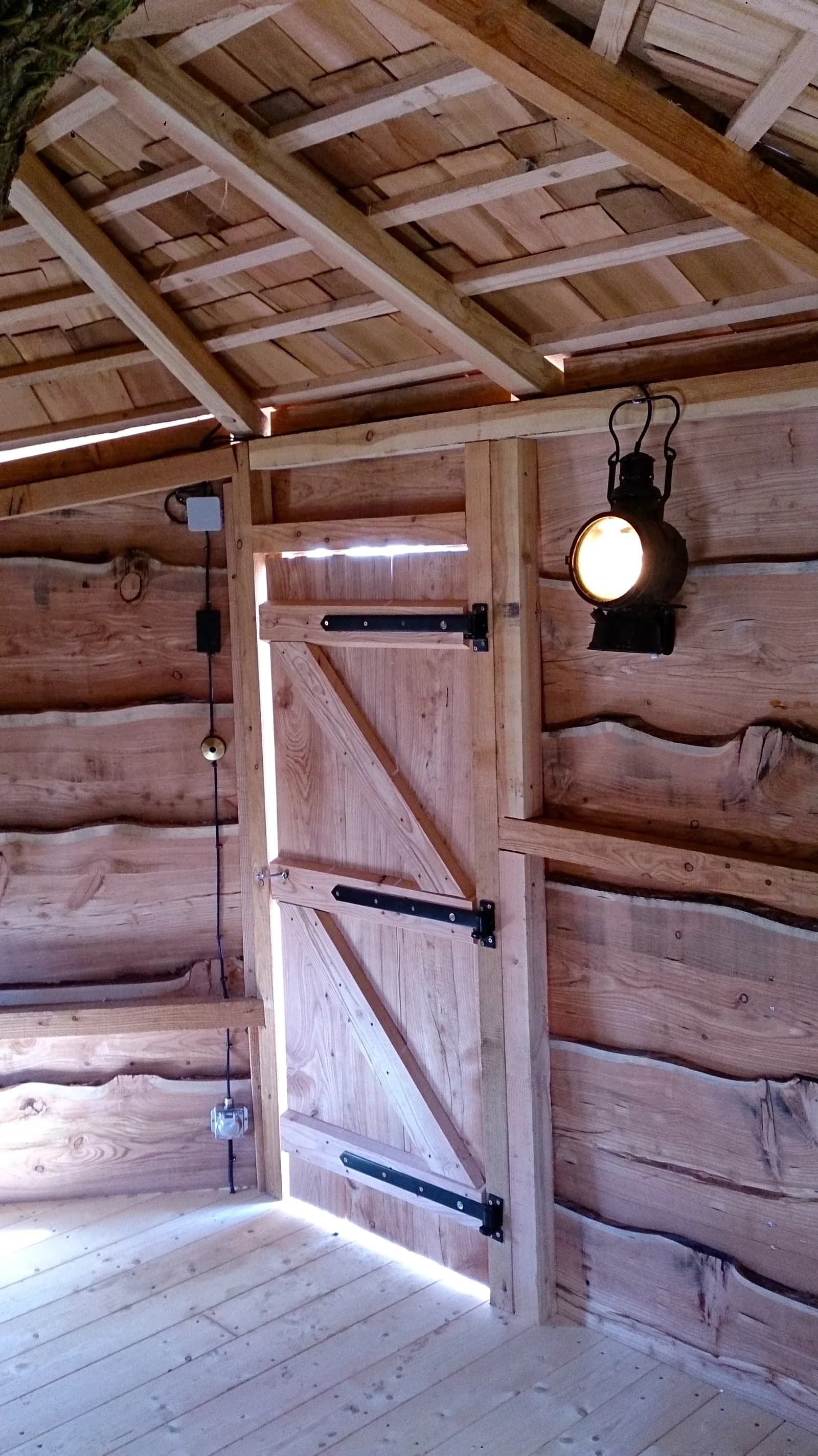 Intérieur d’une cabane en madriers construite par la maison : charpente apparente et porte ferrée